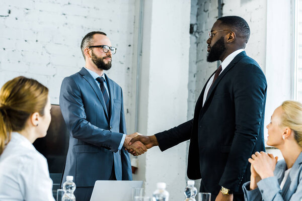 multicultural businessmen shaking hands near coworkers in office 