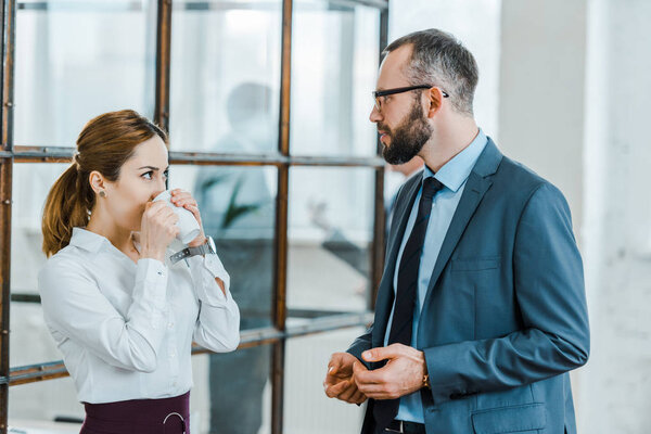 handsome bearded businessman looking at coworker drinking coffee in office 