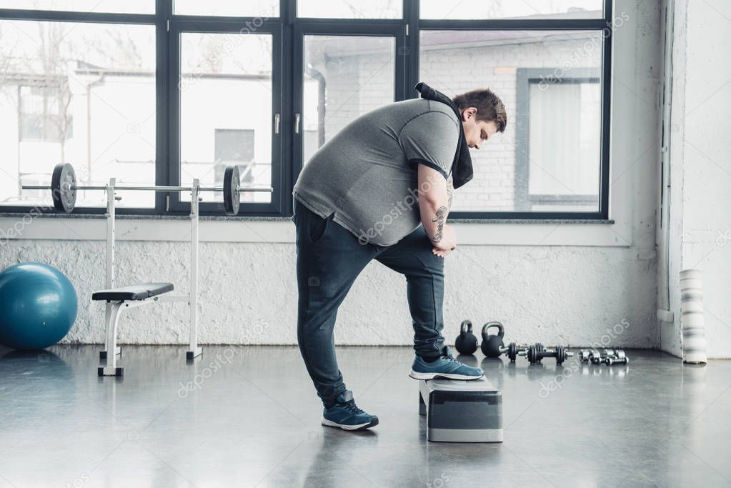overweight man with towel exercising on step platform at sports center