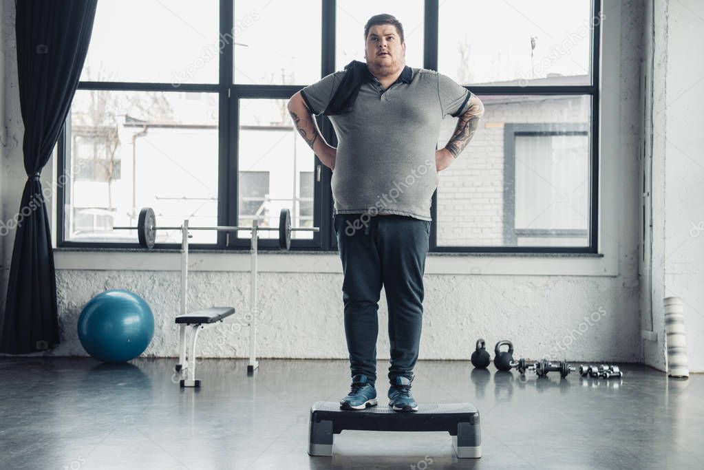 overweight man with towel standing on step platform at sports center