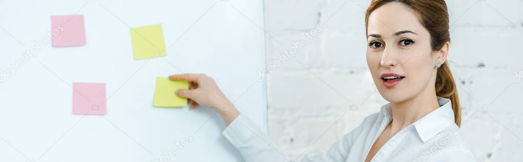 panoramic shot of attractive business coach putting sticky notes on white board 