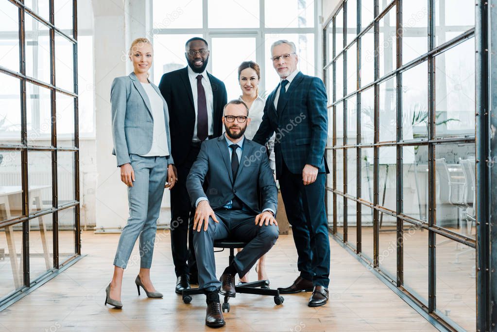 handsome bearded businessman sitting on chair near multicultural coworkers 