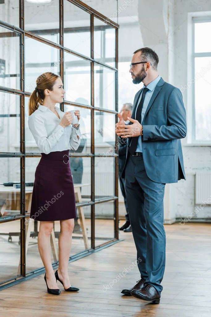 handsome bearded businessman looking at businesswoman holding cup of coffee in office 