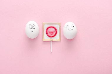 kopya alanı ile pembe lolipop olarak sarılmış prezervatif ile mutlu ve sürpriz yüz ifadeleri ile yumurta üst görünümü