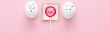 pembe üzerinde lolipop olarak sarılmış prezervatif ile mutlu ve sürpriz yüz ifadeleri ile yumurta panoramik çekim