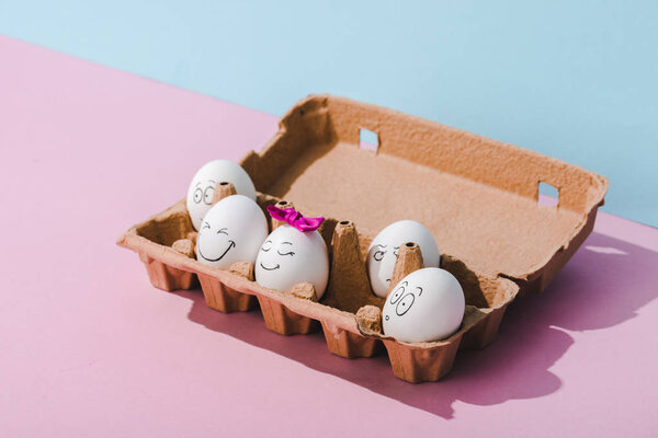 eggs with various face expressions in egg carton on blue and pink