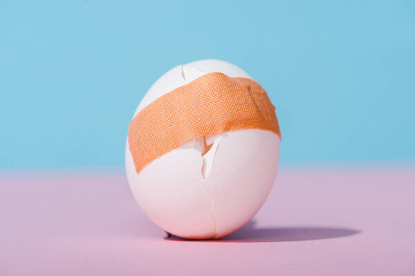 cracked egg with adhesive medical plaster on blue and pink