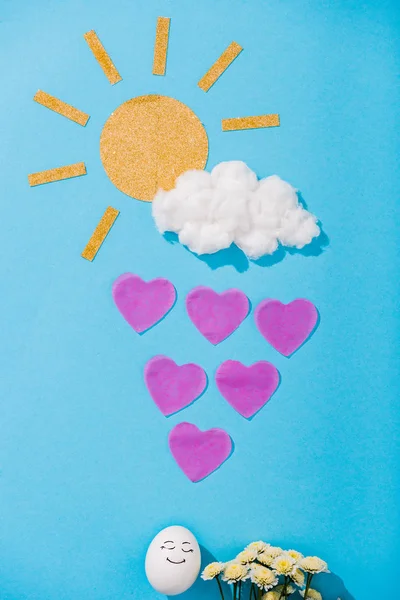 紙の太陽 綿菓子の雲 幸せな顔の表情を持つ卵 花と青のハート型の雨滴のトップビュー — ストック写真