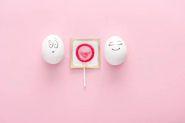 コピースペースでピンクのロリポップとして包まれたコンドームで幸せで驚いた顔の表情を持つ卵のトップビュー — ストック写真