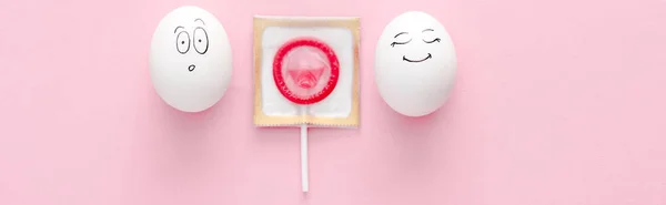 ピンクのロリポップとして包まれたコンドームで幸せで驚いた顔の表情を持つ卵のパノラマショット — ストック写真