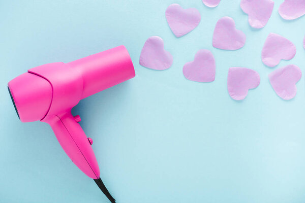 top view of hair dryer blowing paper hearts on pink