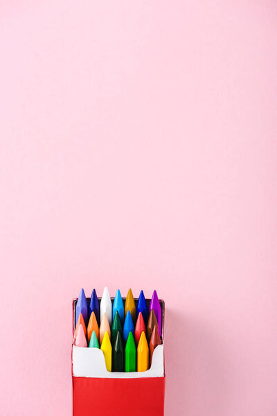 top view of multicolored crayons in cigarette pack on pink with copy space, smoking concept