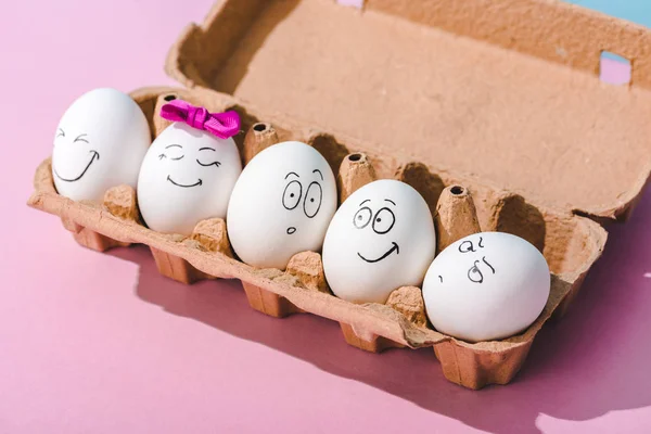 鸡蛋与不同的脸表情在鸡蛋纸箱粉红色 — 图库照片