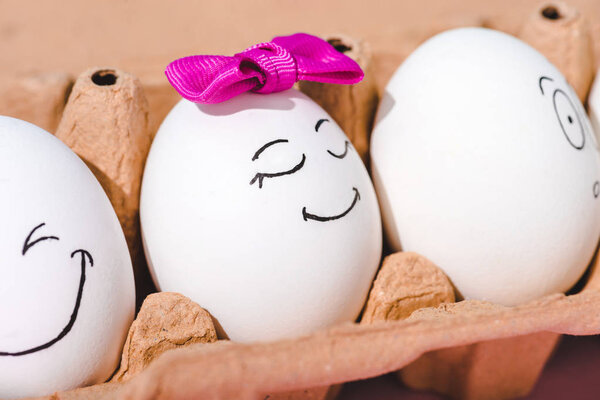 close up view of eggs with different face expressions in egg carton
