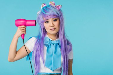 Front view of serious asian anime girl in wig holding hairdryer isolated on blue clipart