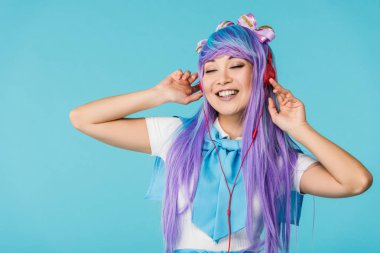 Smiling anime girl in purple wig listening music in headphones isolated on blue clipart
