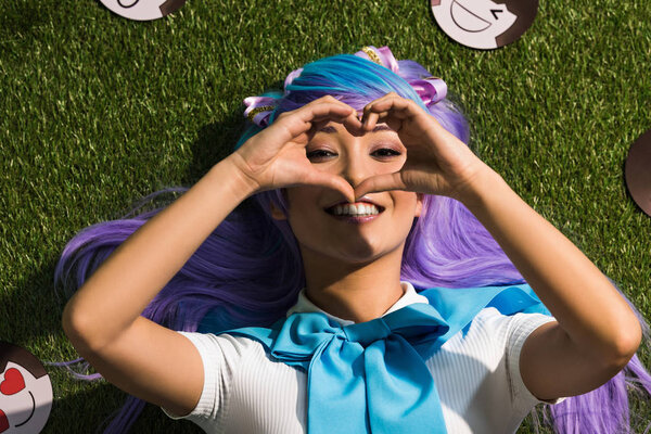 Smiling asian anime girl lying on grass and showing heart sign