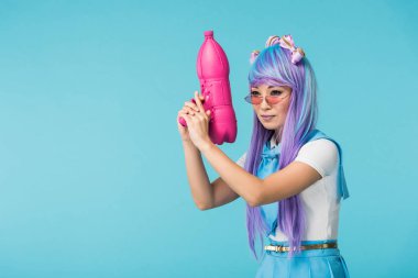 Asian anime girl in wig and glasses holding water gun isolated on blue clipart
