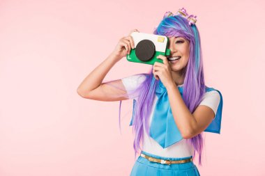 Smiling asian anime girl in purple wig holding cardboard camera isolated on pink clipart