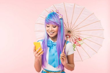Asya anime kız kağıt şemsiye tutan ve pembe izole akıllı telefon kullanarak