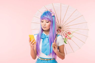 Asian anime girl holding paper umbrella and using smartphone isolated on pink clipart