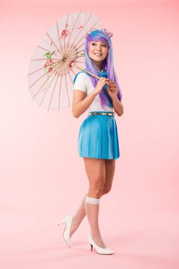 Pembe üzerinde kağıt şemsiye tutan gülümseyen asya anime kız tam uzunlukta görünümü