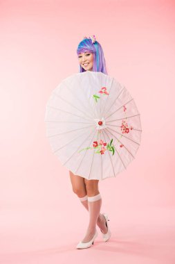 Pembe üzerinde kağıt şemsiye tutan gülümseyen asya anime kız tam uzunlukta görünümü