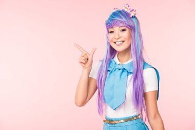Smiling asian anime girl in purple wig pointing with finger isolated on pink clipart