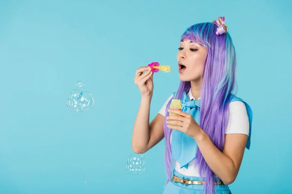 Asian anime girl in purple wig with soap bubbles isolated on blue