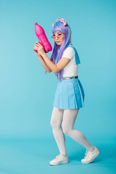 Full length view of asian anime girl in wig and glasses holding water gun on blue