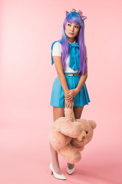 Full length view of asian anime girl holding teddy bear on pink