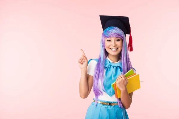Uśmiechnięta Azjatycka Dziewczyna Anime Akademickiej Czapce Trzymając Książki Wskazując Palcem — Zdjęcie stockowe