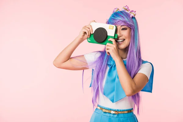 微笑的亚洲动漫女孩在紫色假发拿着纸板相机隔离在粉红色 — 图库照片