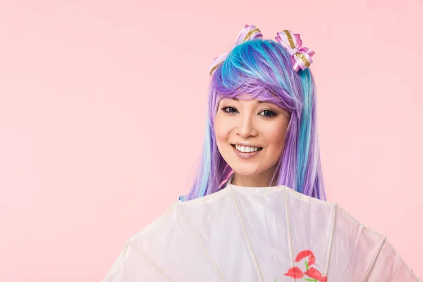 微笑的亚洲动漫女孩在假发拿着纸伞隔离在粉红色 — 图库照片