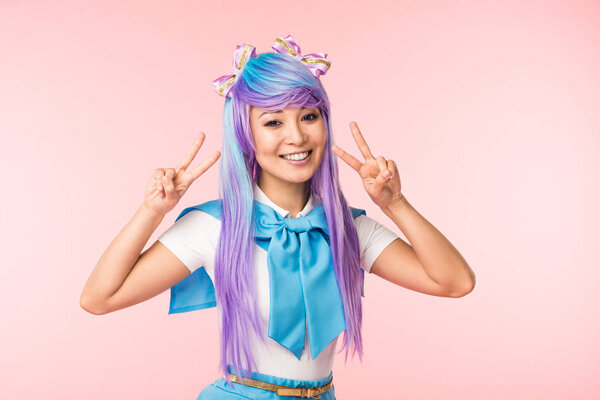 Радостная азиатская девушка аниме в фиолетовом парике показывает знаки мира изолированы на розовый
