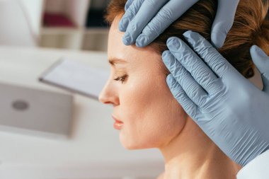 cropped view of dermatologist in latex gloves examining hair of attractive patient in clinic  clipart