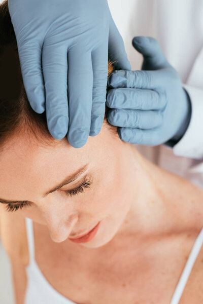 обрезанный вид дерматолога в латексных перчатках, осматривающих волосы пациента
 