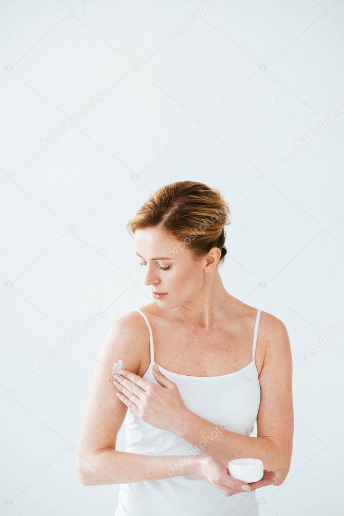 attractive woman with skin illness holding container and applying cosmetic cream on white 