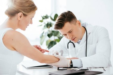 handsome dermatologist examining hand of attractive woman while holding dermatoscope  clipart