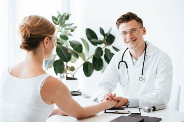 gözlük ve beyaz ceket hasta ile el ele tutuşan neşeli doktor seçici odak 