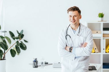 Klinikte kolları çapraz duran beyaz önlüklü neşeli doktor. 