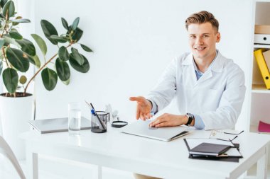 Klinikte dizüstü bilgisayarın yanında otururken neşeli doktor hareketi 