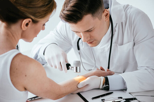 selective focus of dermatologist examining hand of woman with dermatoscope 