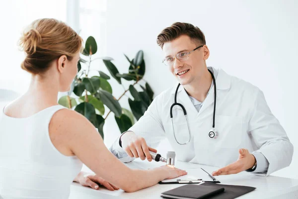 Dermatólogo Alegre Sosteniendo Dermatoscopio Sonriendo Mientras Mira Paciente —  Fotos de Stock