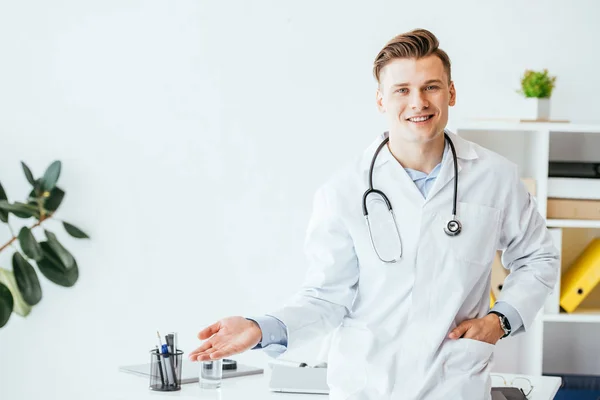 穿着白色外套的快乐的医生手插在口袋里站着 在诊所里为自己做手势 — 图库照片