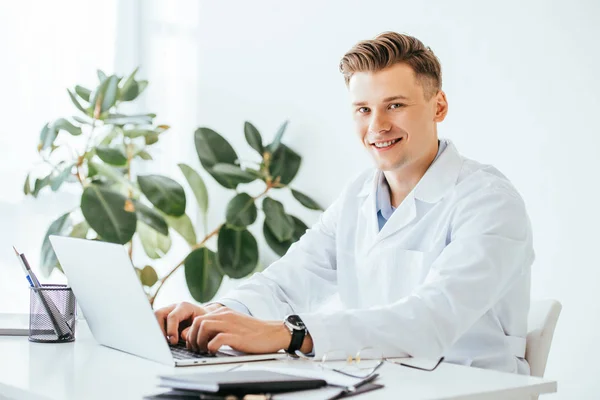 Zufriedener Arzt Schaut Die Kamera Während Laptop Der Klinik Benutzt — Stockfoto