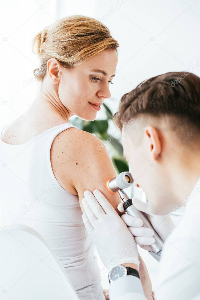 dermatologist in latex gloves holding dermatoscope while examining beautiful patient with skin disease  
