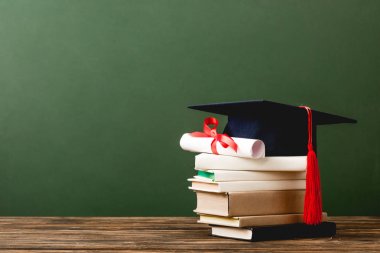 yeşil izole ahşap yüzey üzerinde kitap, akademik kap ve diploma