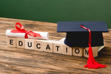 Ahşap zemin üzerinde harf, akademik kapak ve diploma bulunan tahta bloklar yeşil üzerine izole edilmiş.