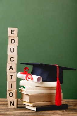 Ahşap yüzey üzerinde harf, kitap, akademik kapak ve diploma bulunan tahtadan bloklar yeşil üzerine izole edilmiş.